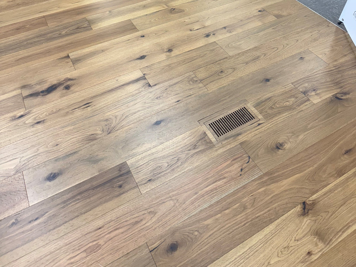 Flush floor vent cleanly set into a light oak hardwood floor in a flooring showroom