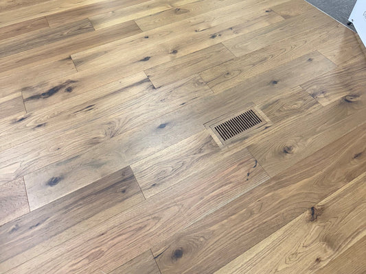 Flush floor vent cleanly set into a light oak hardwood floor in a flooring showroom