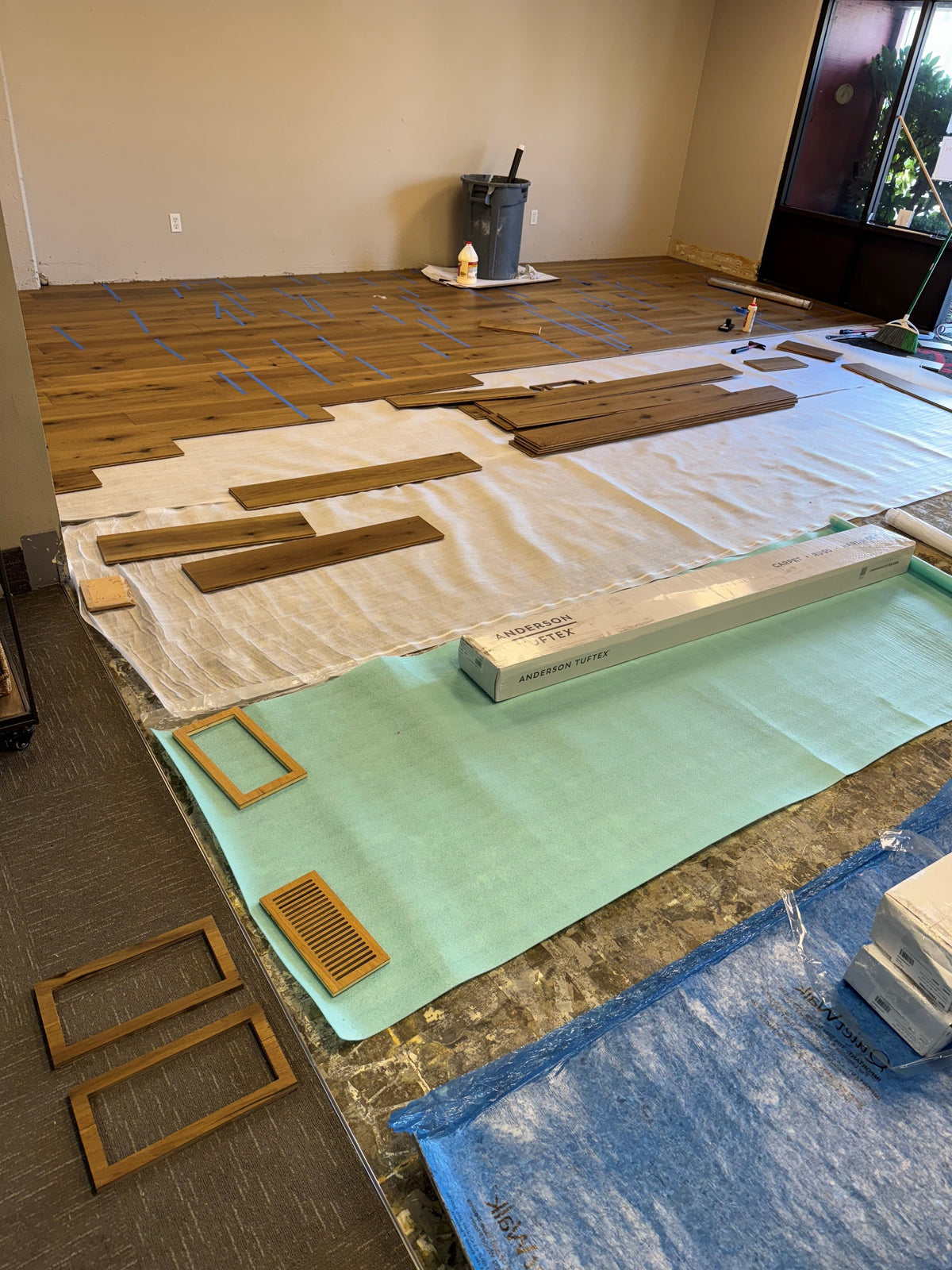 Engineered hardwood install in progress, with flush vent frames and a matching vent laid out on the underlayment before the planks go in
