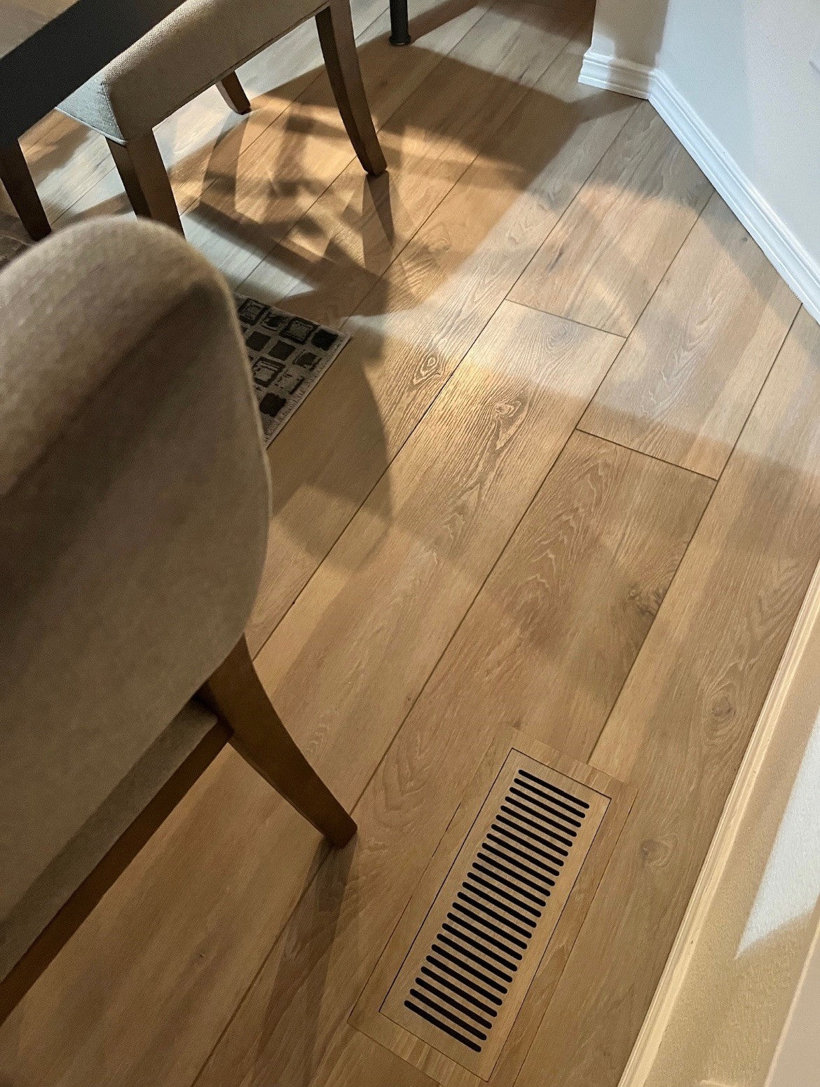 Flush slotted floor vent made from matching wood-look plank, installed next to a dining chair