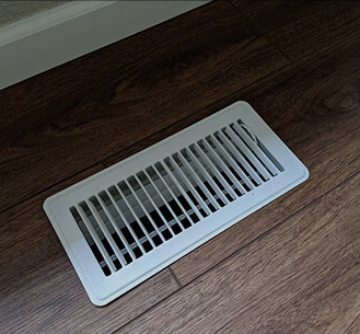 Painted white metal floor register on a wood floor, the look a matching vent replaces