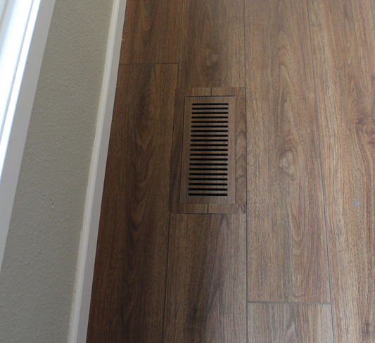 Standard size flush floor vent cover in a dark wood-look floor