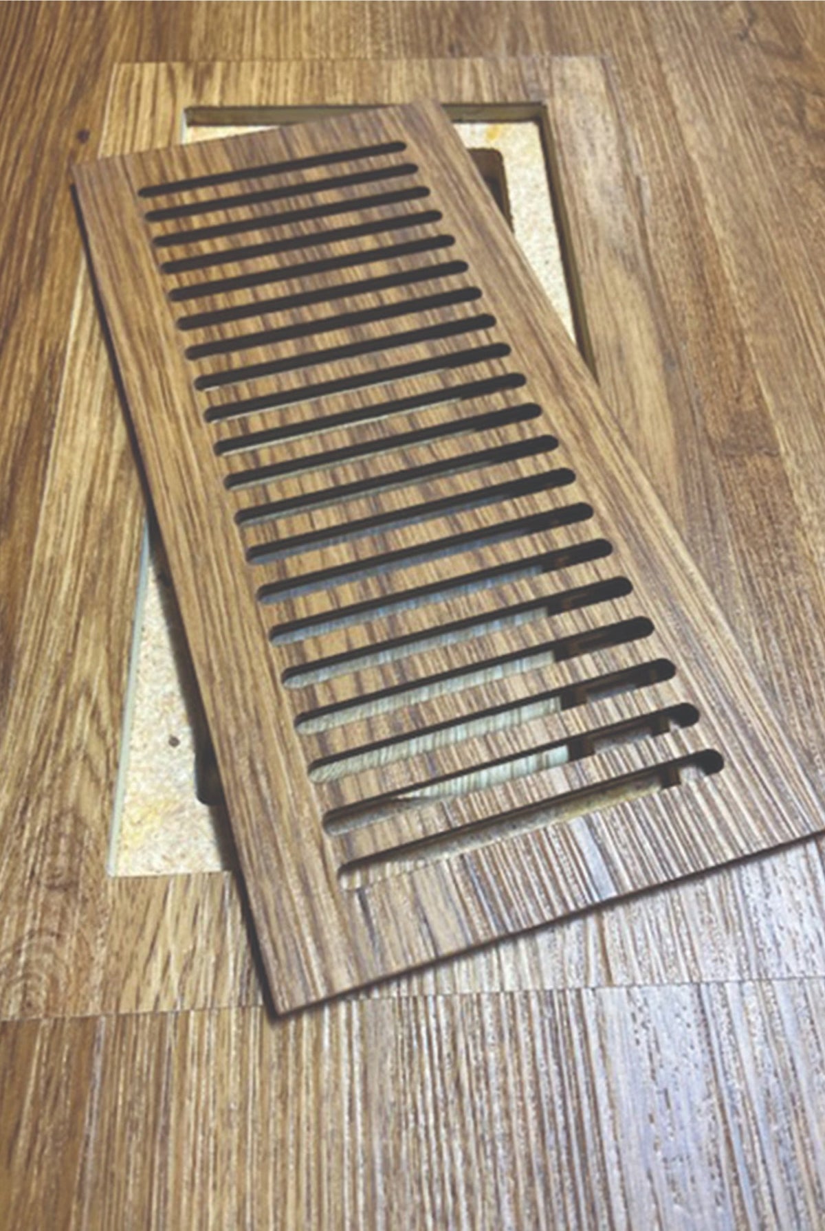 Custom flush floor vent made from wood-look vinyl plank, lifted from its frame in the matching floor
